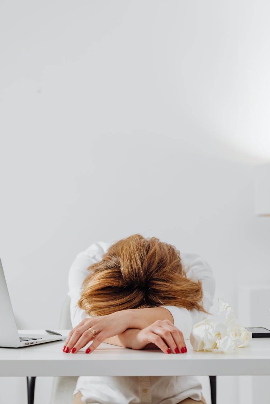 A person resting their head on a white desk. Its implyed they are suffering from autistic burnout.